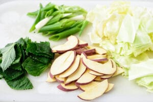 Perilla leaves, scallions, cabbage, and Korean sweet potato cut into bite size pieces on a cutting board