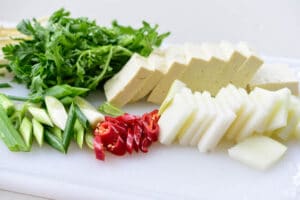 Cutting Korean radish, scallions, red chili pepper, and and tofu on a cutting board